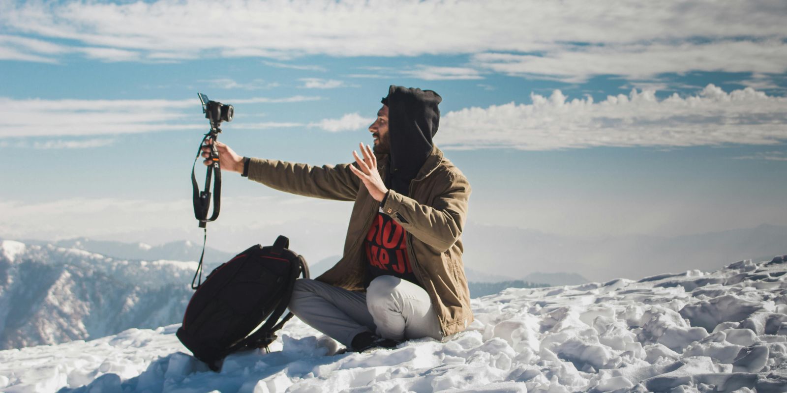 A traveler sets up a camera to capture a video in a snowy mountainous landscape, expressing joy and excitement.