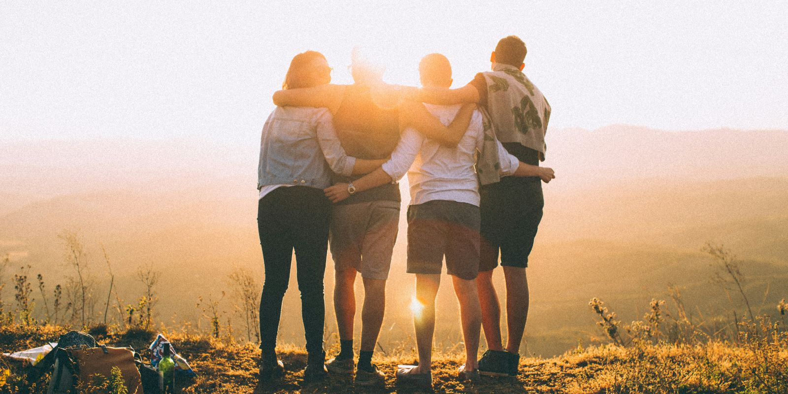 4 people wrapping hands on each other while standing on top of a mountain