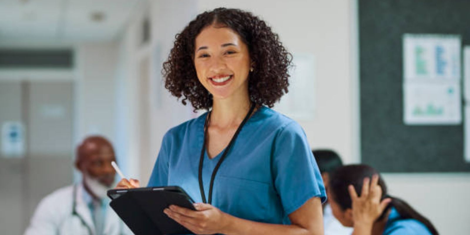 Female nurse with curly hair holding digital tablet, smiling cheerfully at camera