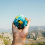 a person holding a mini globe on his hand on top of a mountain