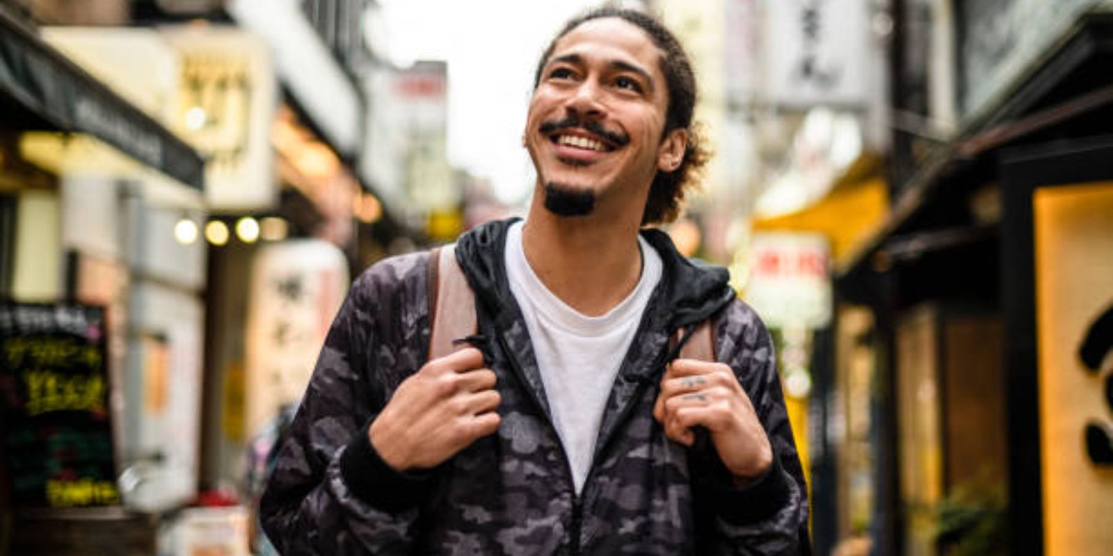 Male traveller carrying backpack exploring new city and smiling