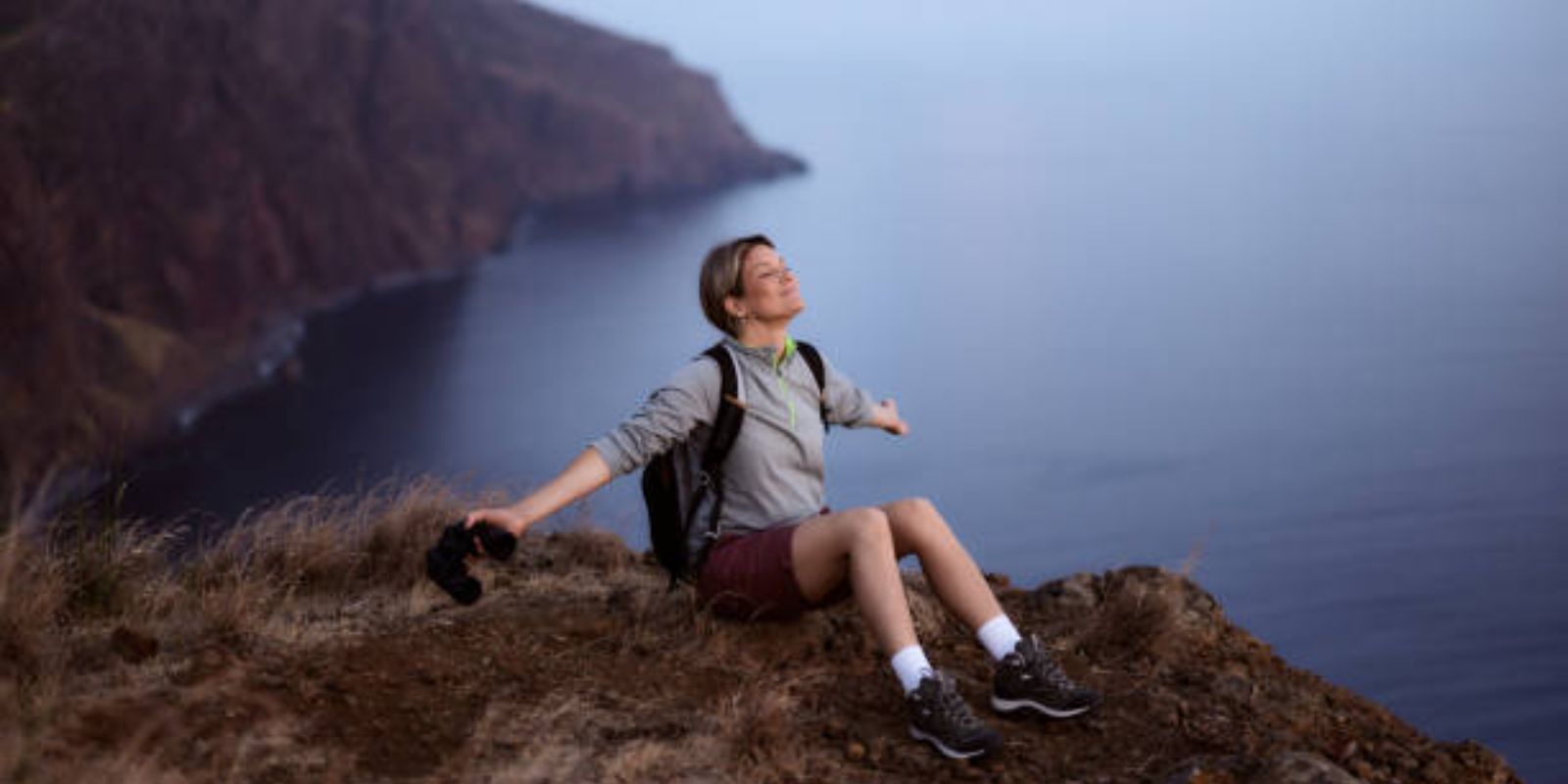 Smiling female relaxing with outstretched arms from her hike on a mountain