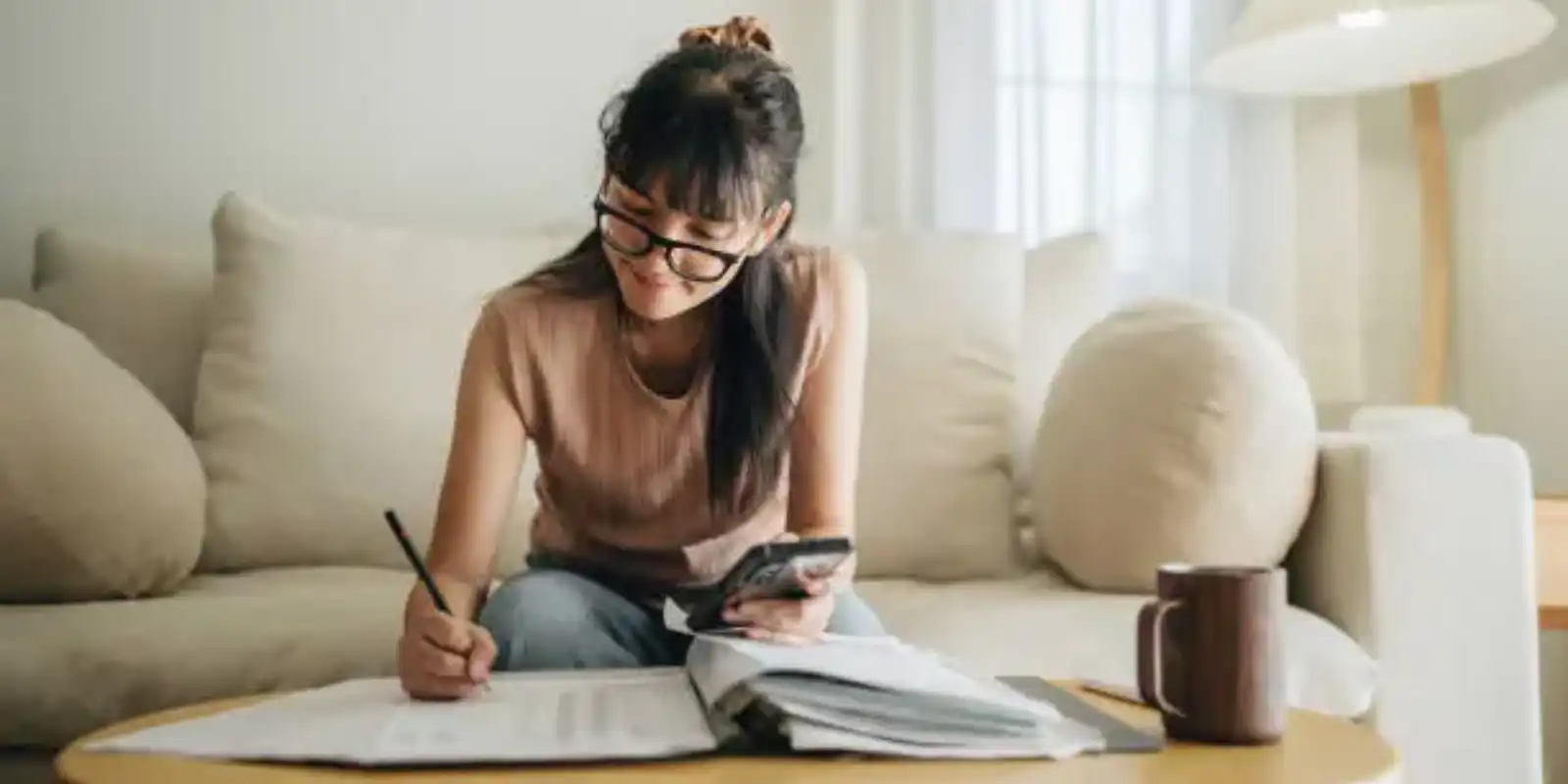 A woman sits at her living room with smartphone and financial reports