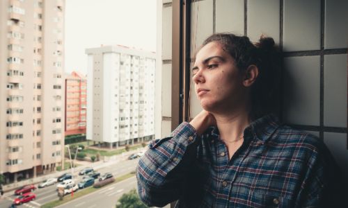 A woman leaning against a wall, looking out of a window.