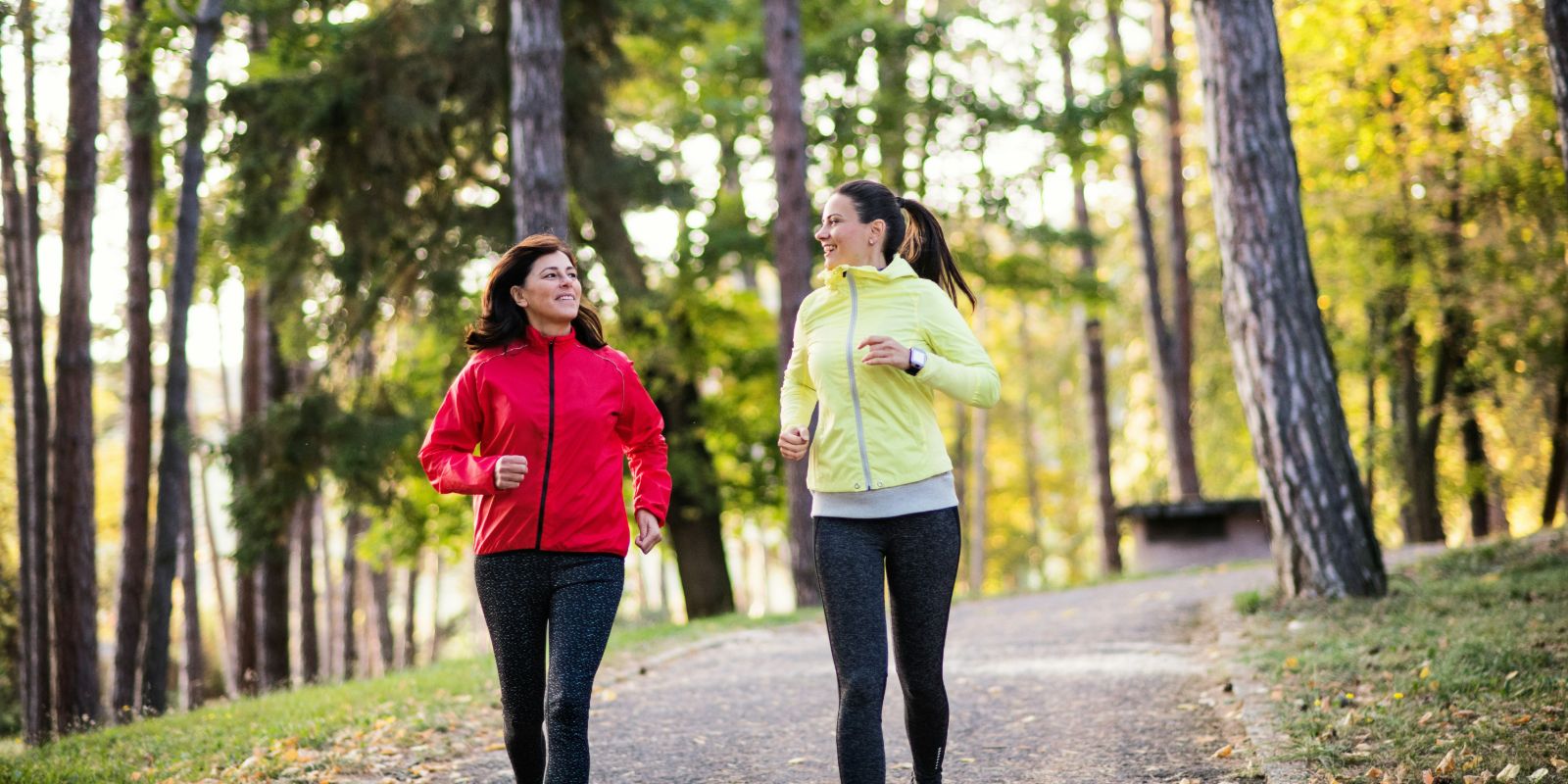 Two active female runners are jogging outdoors in a forest.