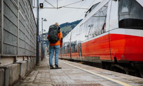 Backpacker waiting at a train station, embracing travel on a sustainable gap year.