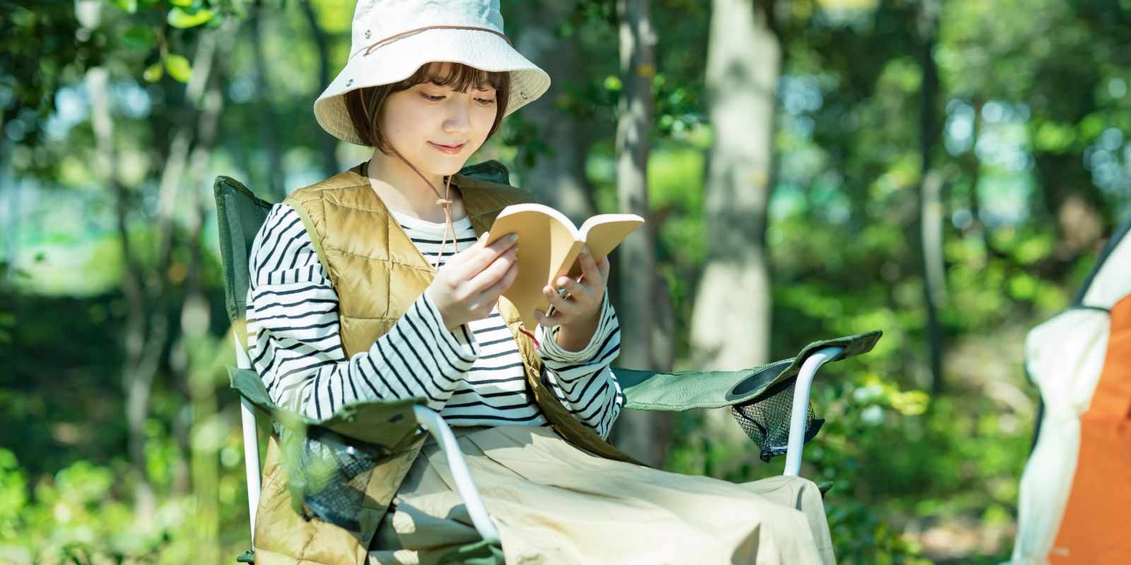 Young woman reading a book at a forest campsite.